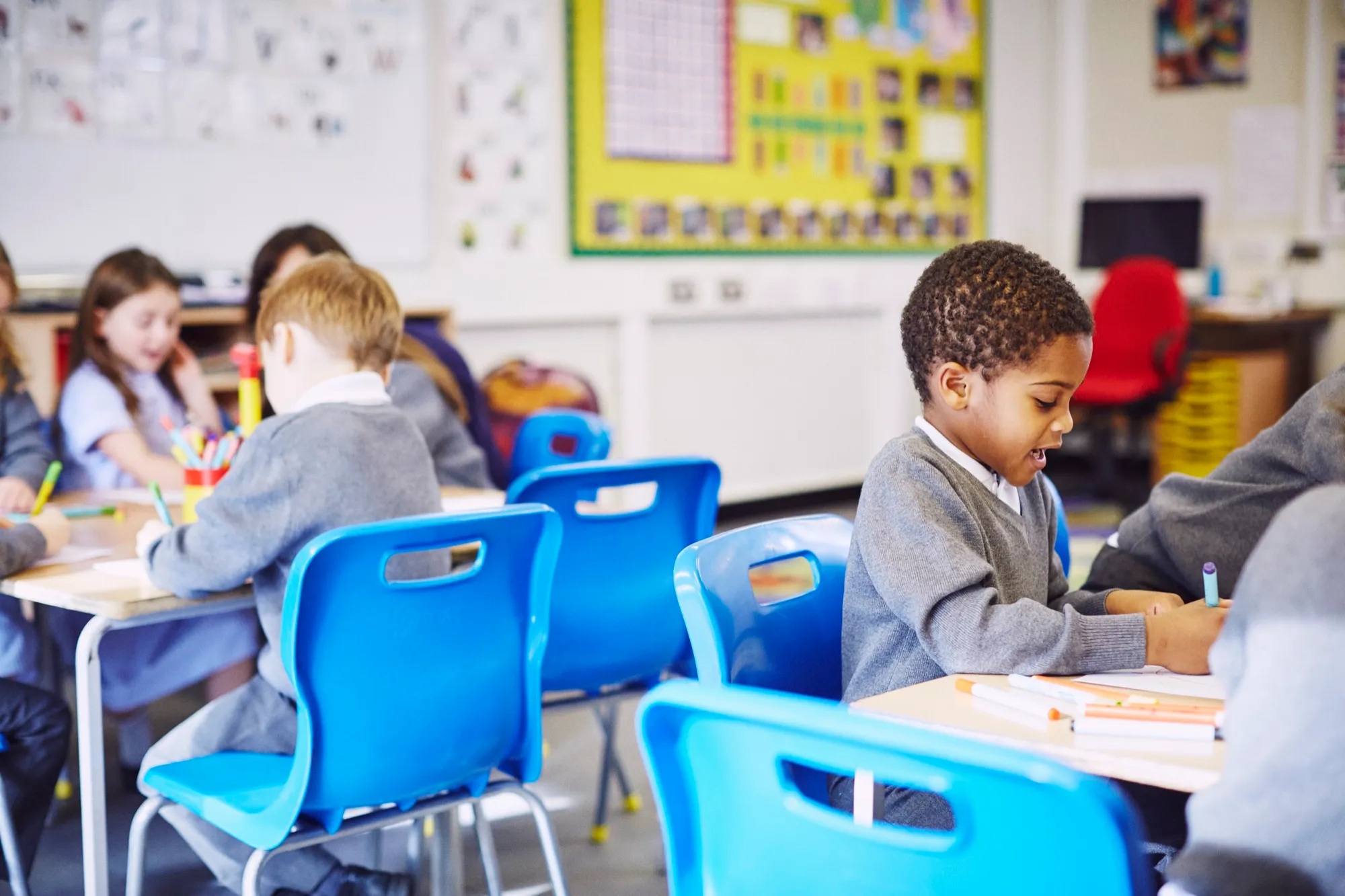 Children in school uniform working at desks in a primary classroom.