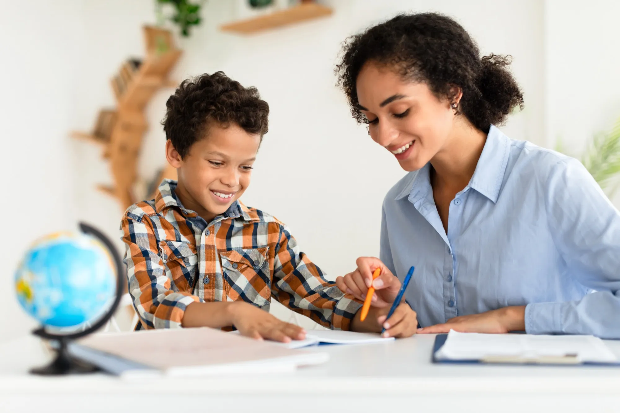 A tutor and a smiling boy working together at a desk with a globe beside them.